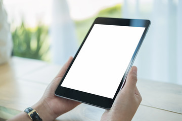 Mockup image of hands holding black tablet pc with blank white screen on wooden table in cafe