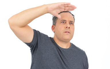 Man puts his hand on his forehead to see further. He is bald, has overweight and wears dark gray T-shirt..