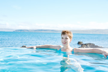 Young cheerful girl swimming in water of pool looking away on background of sea, Iceland, West Fjords.