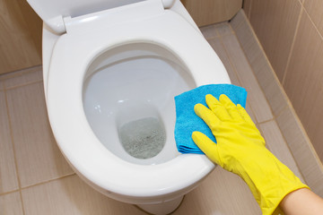 A hand in a yellow glove washing a toilet bowl