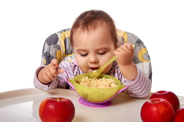 Fototapeta premium little child eats with spoon sitting at table with fruits isolated