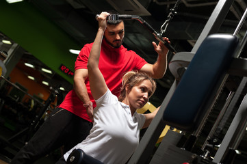 Fototapeta na wymiar Young male coach assisting female client in gym