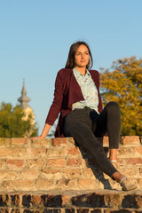 Naklejka na ściany i meble a beautiful girl poses in front of a medieval fortress at sunset
