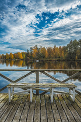 Picture of blue sky over autumn lake and wooden pier with the bench.