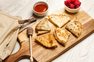 Crepes caseras junto a frambuesas naturales y un cuenco con miel sobre una tabala de madera rústica. Vista superior
