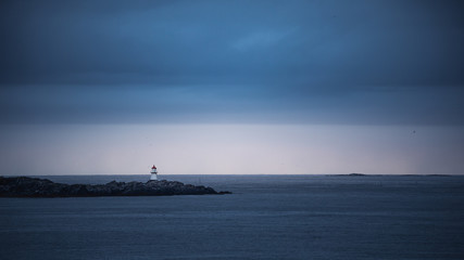 Obraz premium Little lighthouse on rocks surrounded by an ocean against cloudy sky
