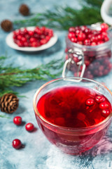 A fresh juicy drink made from cranberry berries in a glass cup on a blue marble background with spruce branches and cones with a copy of the space