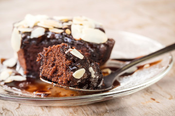 Closeup homemade brownie on glass plate. Sliced brownie on spoon. Served with almond sliced topping and chocolate sauce. Sweet and moist dessert.
