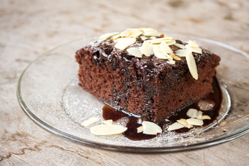 Closeup homemade brownie on glass plate.  Served with almond sliced topping and chocolate sauce. Sweet and moist dessert.