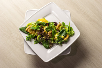  Green salad with fruits on a white square plate on a bright table