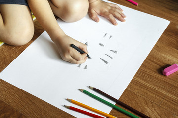 Girl draws picture with crayons on the sheet of paper on the floor