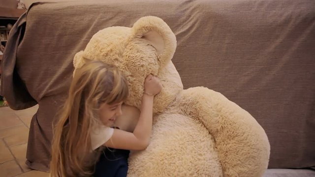 A cute little girl jumping on her toy, a giant teddybear, and hugging him. Funny lifestyle shot. Jump from the left.
