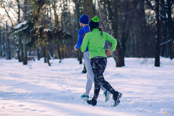 Fototapeta na wymiar Happy young couple in winter running and doing exercises. Runners jogging in snow. Young asian woman fitness model and caucasian man.