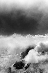 Black and white snowy mountains in sunlight clouds before snow storm