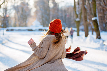Young gorgeous lady  in a warm hat and scarf walking  with thermocup in hands on the background of the  winter park.