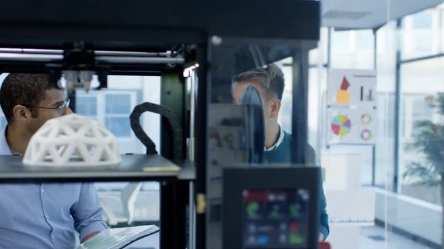 Engineers looking at prototype in a 3D printer and checking design on computer