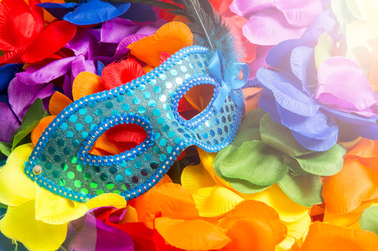 Sequined blue carnival mask sits on bright background of rainbow colored flower leis