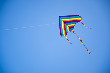 Colorful rainbow striped kite flying in a clear blue sky