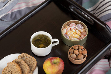 Breakfast in bed - cup of tea, bread, candy, apple and nuts on wooden tray