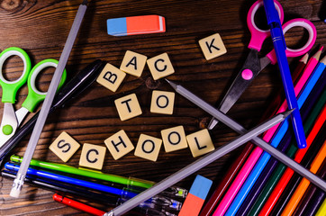Set of the different school stationeries. Pens,  scissors, pensils, eraser on wooden desk. Back to school inscription. Top view