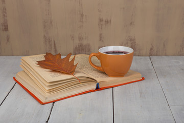 Concept of autumn resting - cup of tea with autumn colorful leaves and book on white wooden table and brown background