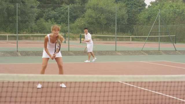  Mixed doubles tennis players enjoying a game on outdoor court in the summer.