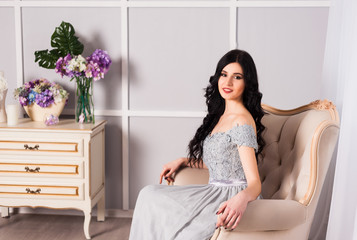 young woman in elegant blue gray evening dress indoors with beautiful interior