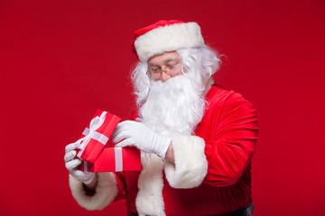 Christmas. Photo Santa Claus giving xmas present and looking at camera, on a red background