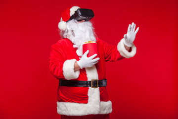 Santa Claus wearing virtual reality goggles and a red bucket with popcorn, on a red background. Christmas