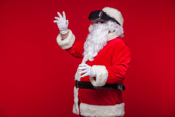 Santa Claus wearing virtual reality goggles, on a red background. Christmas