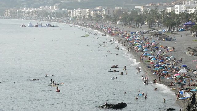 Landscape of mediterranean beach with crowd of people bathing in summer at sunset