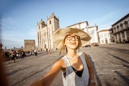 Young woman tourist making selfie photo with phone standing in front of the main cathedral in Porto city during the sunset in Portugal