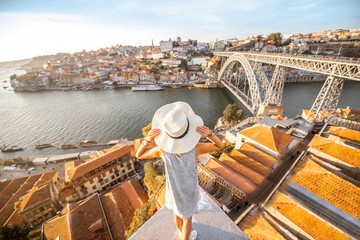 Young woman tourist enjoying beautiful landscape view on the old town with river and famous iron bridge during the sunset in Porto city, Portugal - obrazy, fototapety, plakaty