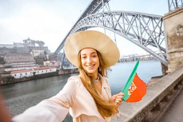 Portrait of a young woman traveler with portuguese flag on the famous iron bridge background in Porto city