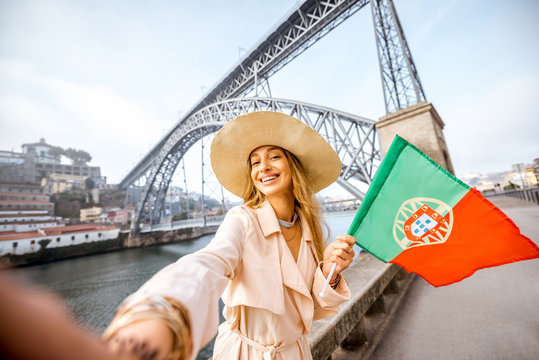 Portrait of a young woman traveler with portuguese flag on the famous iron bridge background in Porto city