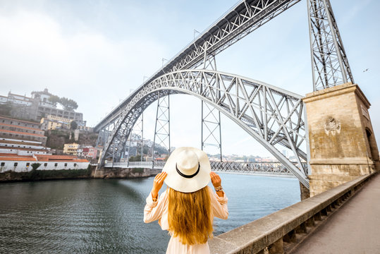 Beautiful woman in hat enjoying morning view on the famous iron bridge during the foggy weather in Porto city, Portugal