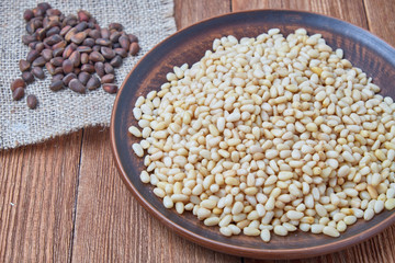 Peeled pine nuts on a plate on a wooden background.