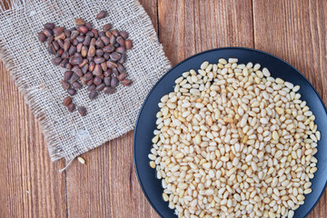 Peeled pine nuts on a plate on a wooden background.