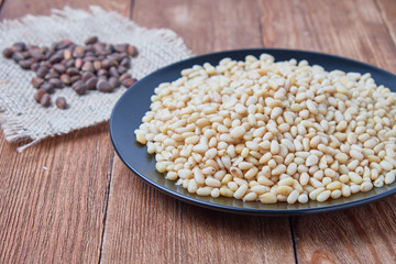 Peeled pine nuts on a plate on a wooden background.