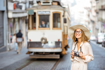 Lifestyle portrait of a woman traveler standing on the street with the famous old touristic tram on the background in Porto city, Portugal