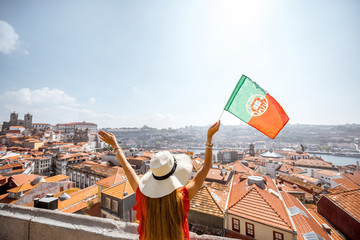 Young woman tourist in red dress standing back with portuguese flag on the old town background...