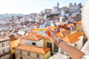 Holding a toy airplane on the Porto cityscape background. Traveling by airplane in Porto concept