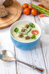 Beautiful asparagus cream soup with toasted bread on white wooden table.