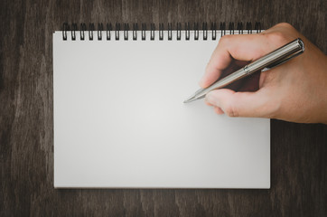 Hand writing with pen on empty notepad on wooden table background