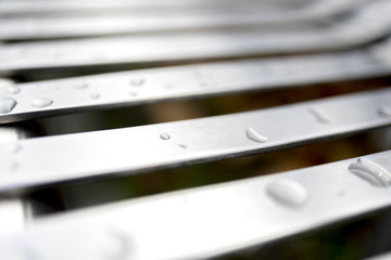 Close up of contemporary modern stainless steel street or park bench with raindrops on that makes an interesting abstract background or architectural feature