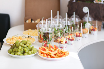 Catering for wedding party. Plenty of mixed various kinds of sliced fruit, vegetables, cheese, salads in plastic cups on table indoors