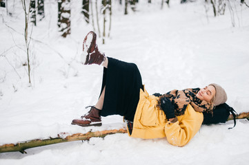Fototapeta na wymiar Odd bizarre female lying on tree in snowy winter forest. Beautiful young lovely girl relaxing outdoor. Unusual woman on vacation resting at nature. Lonely lady traveling in frost cold weather day.