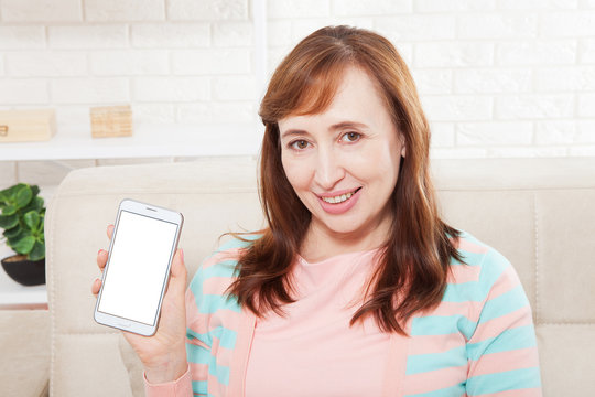 Female Hand Holding White Phone On White Clipping Path Inside At Home Background. Middle Age Woman. Copy Space And Mock Up