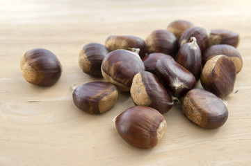Raw sweet chestnuts scattered on a wooden table, tasty and healthy brownish nuts