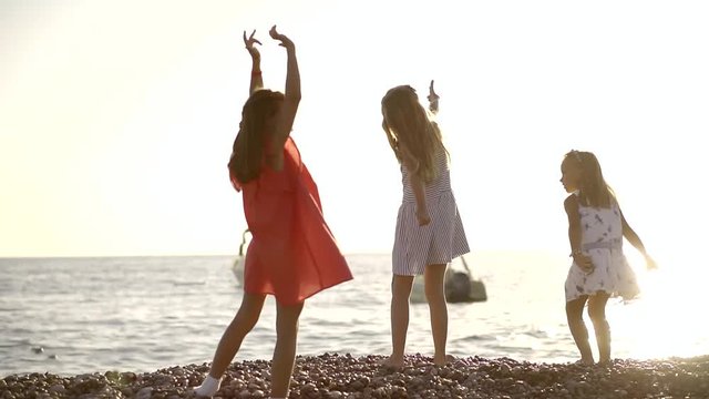 three little girl is playing on a sea shore in summer time, they are throwing stones to a water